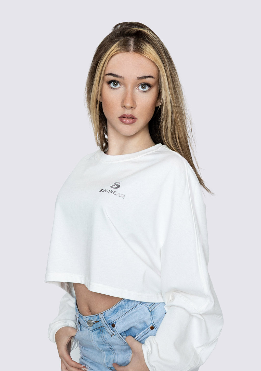 Woman wearing a white oversized t-shirt with a Sin-Wear logo on a plain background