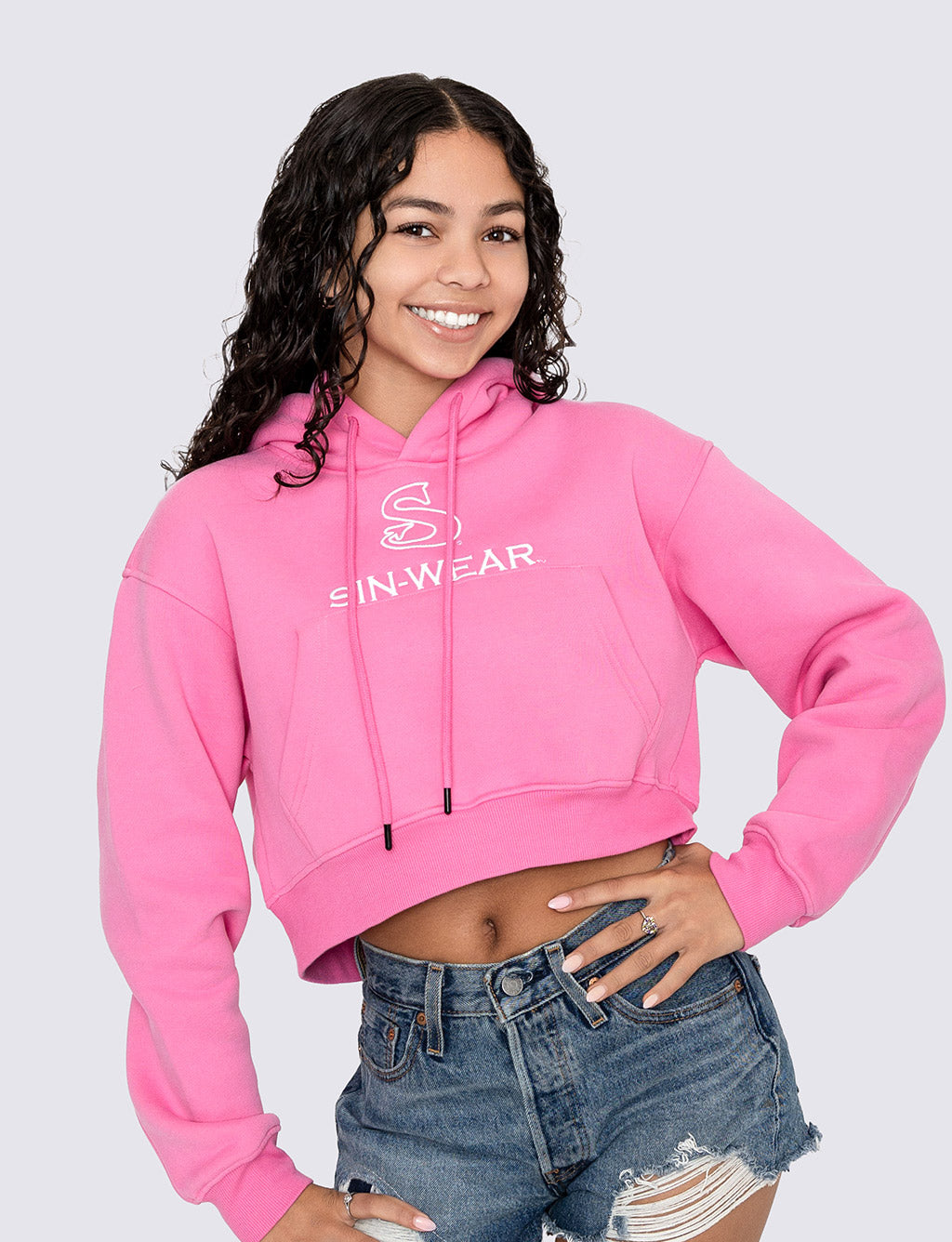 Person wearing a pink crop hoodie with 'Sin-Wear' logo and text, standing against a plain background