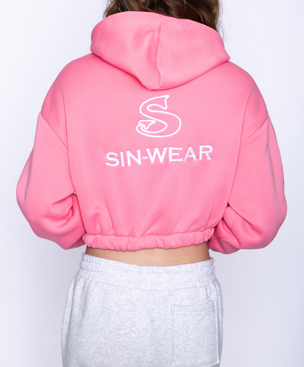 Pink crop zipper hoodie with 'SIN-WEAR' logo on the back against a white background