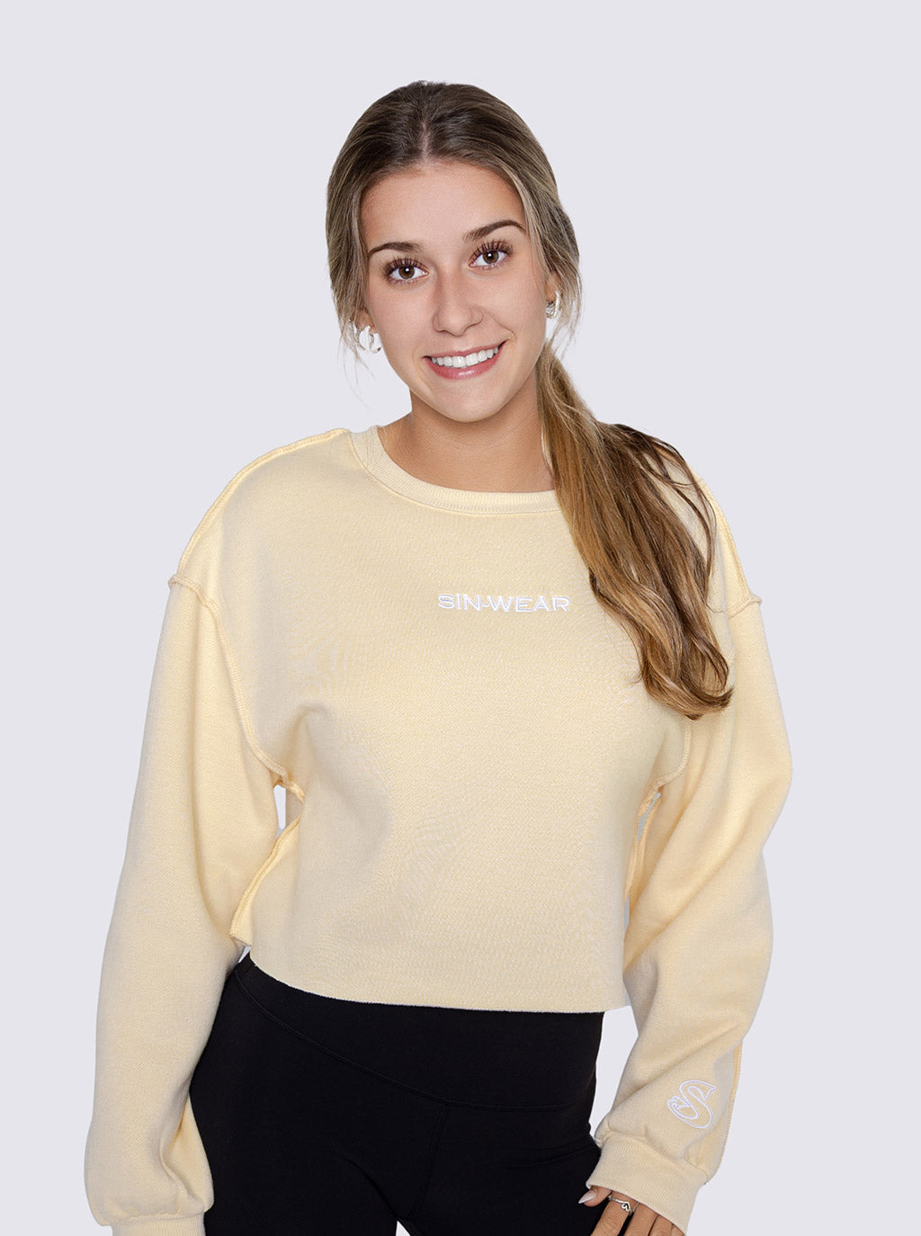 Woman wearing a light yellow crop sweatshirt with Sin-Wear brand logo on a white background
