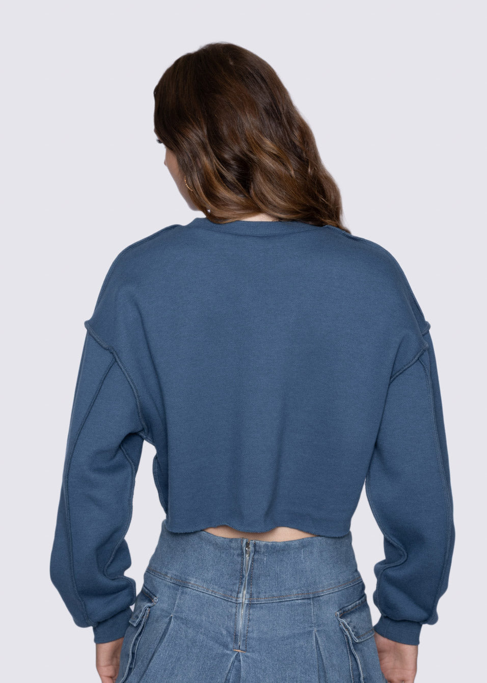 Person wearing a blue cropped sweatshirt and jeans on a white background