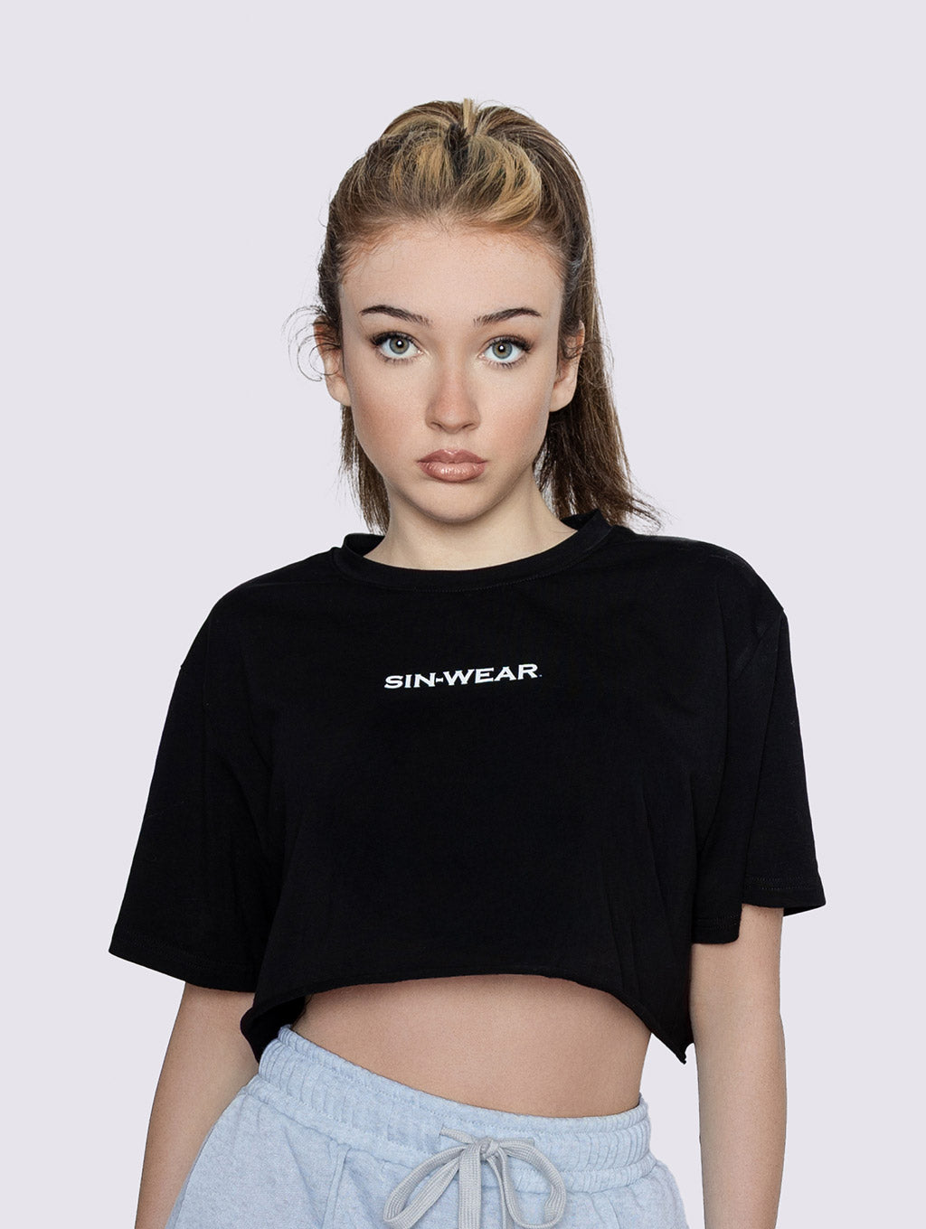 Person wearing a black 'SIN-WEAR' crop top against a plain background