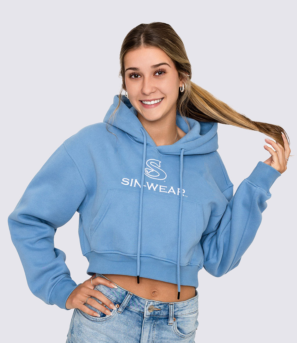 Woman wearing a blue crop hoodie with a 'Sin-Wear' logo on a light gray background