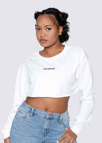 Person wearing a white long-sleeve crop top with 'Sin Wear' branding and blue jeans on a light gray background.
