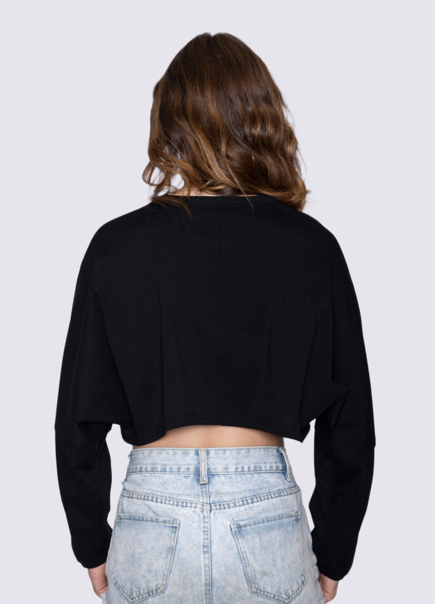 Person wearing a black cropped sweatshirt and light blue jeans on a white background