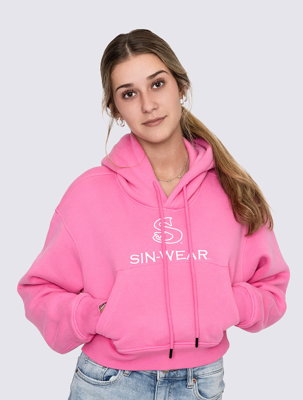 Person wearing a pink crop hoodie with 'SIN-WEAR' logo on a light gray background