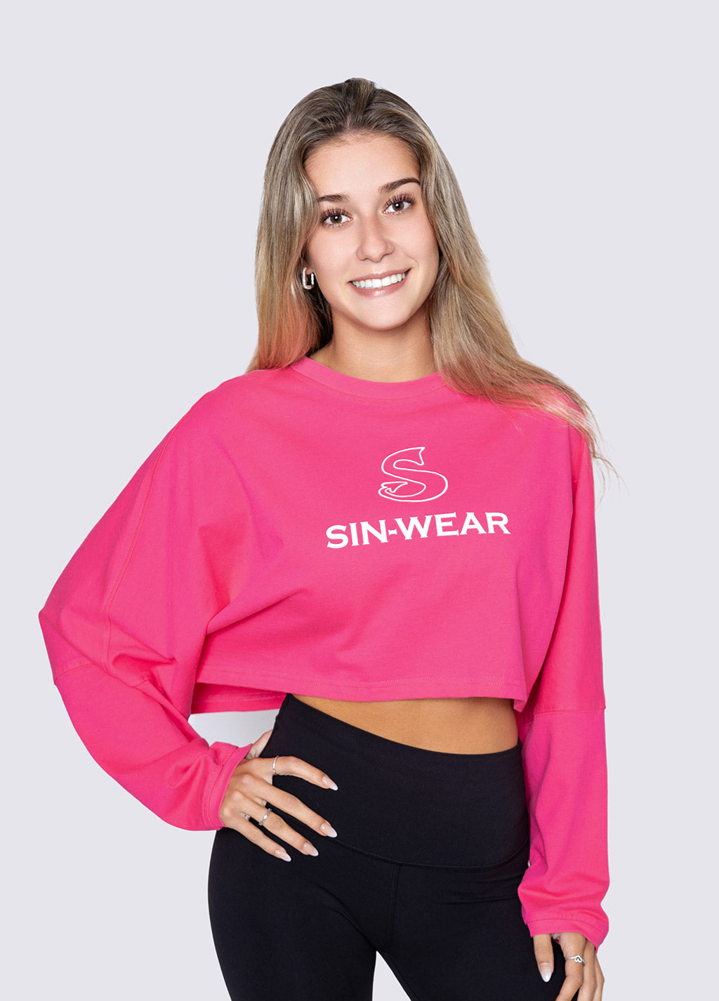Woman wearing a pink 'SIN-WEAR' crop top against a white background