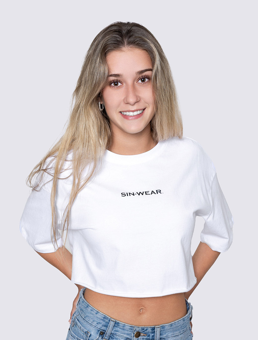 Person wearing a white crop top with 'SIN-WEAR' text on a plain background