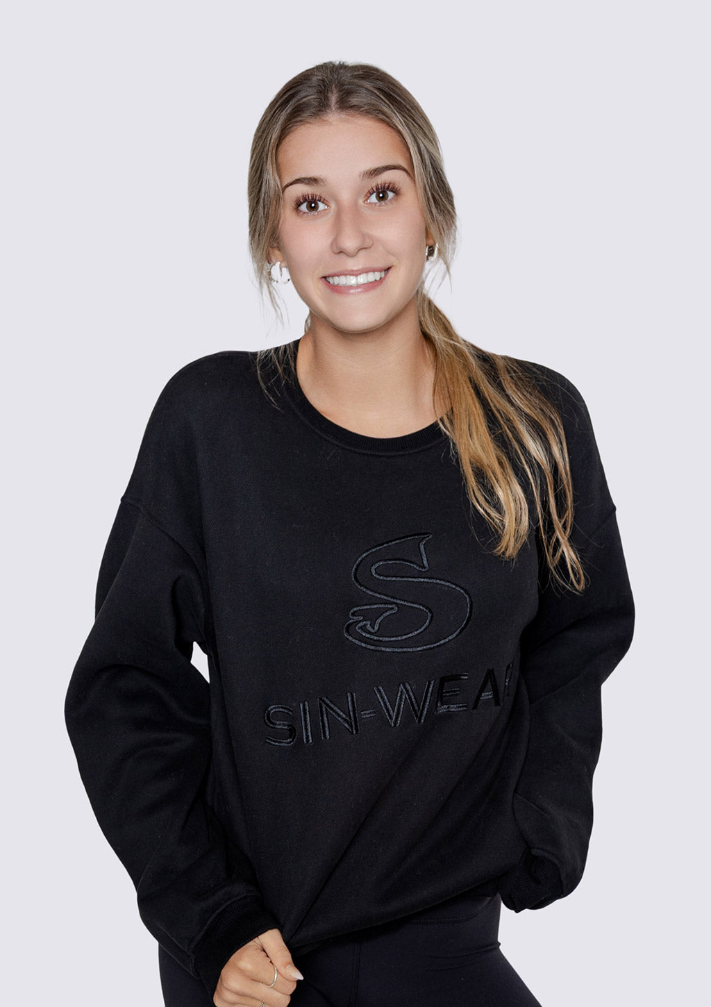 Woman wearing a black sweatshirt with 'SIN-WEAR' branding on a white background