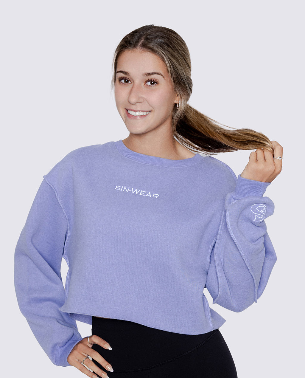 Woman wearing a light purple sweatshirt with 'SIN-WEAR' branding on a plain background