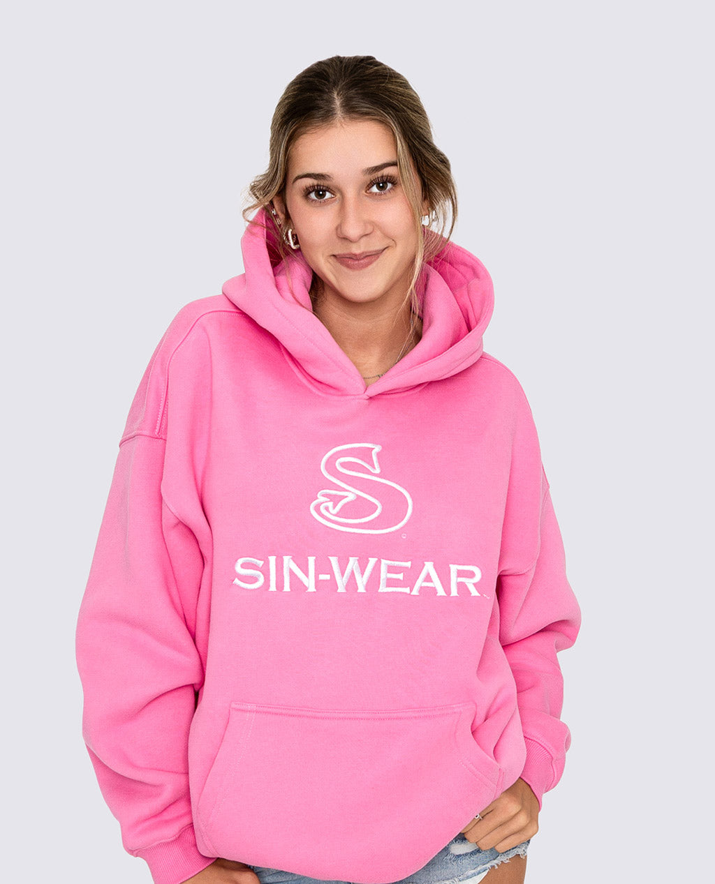 Person wearing a pink hoodie with 'SIN-WEAR' logo on a light gray background