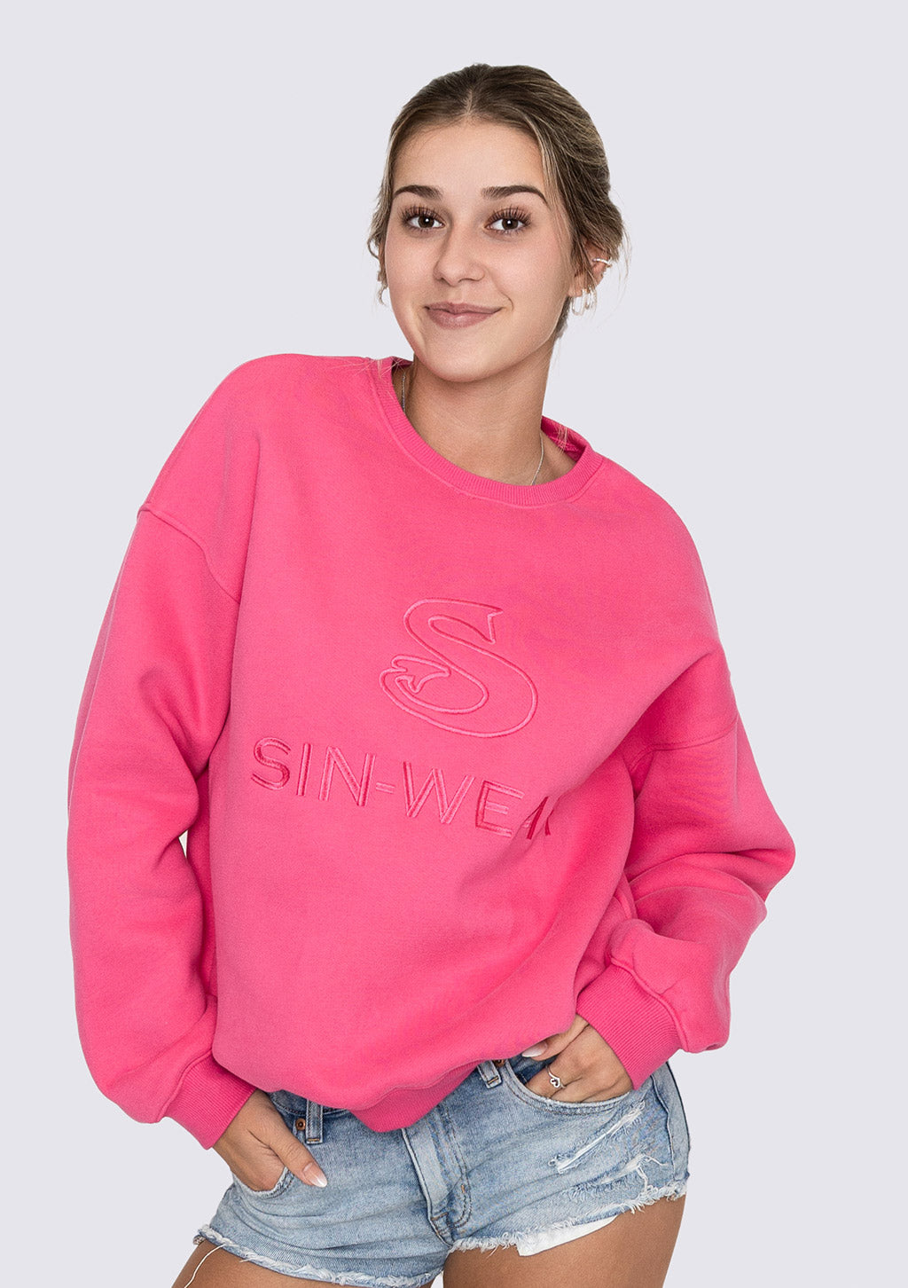 Person wearing a pink sweatshirt with 'SIN-WEAR' text on a plain background