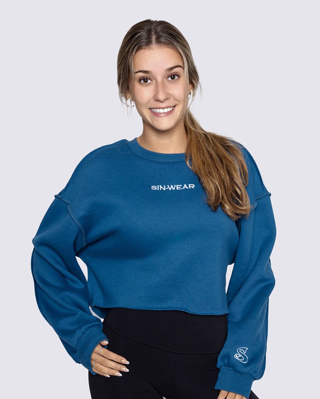 Woman wearing a blue sweatshirt with 'SIN-WEAR' logo on a light gray background